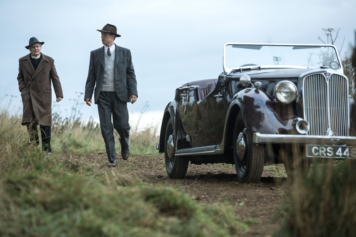 Two men walk near a car on a hill