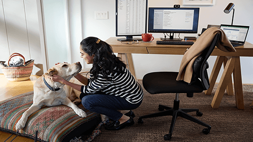 Frau, die kniet, um ihren Hund in einem Heimbüro mit Schreibtisch, Computer und Stuhl zu streicheln