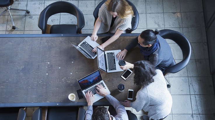 overhead photo of four people working on computers and devices at a table