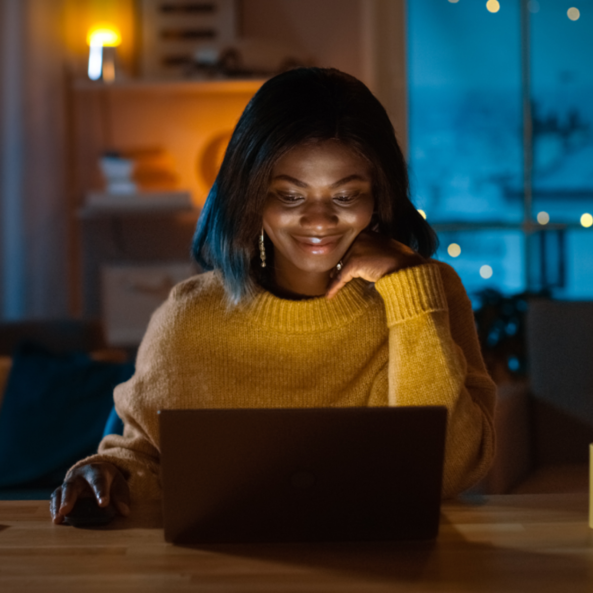 A woman uses her laptop at her table in the evening.