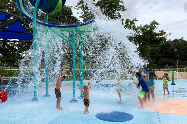 kids getting splashed by the super wave dropping lots of water on top of them at the splash pad at Henderson park