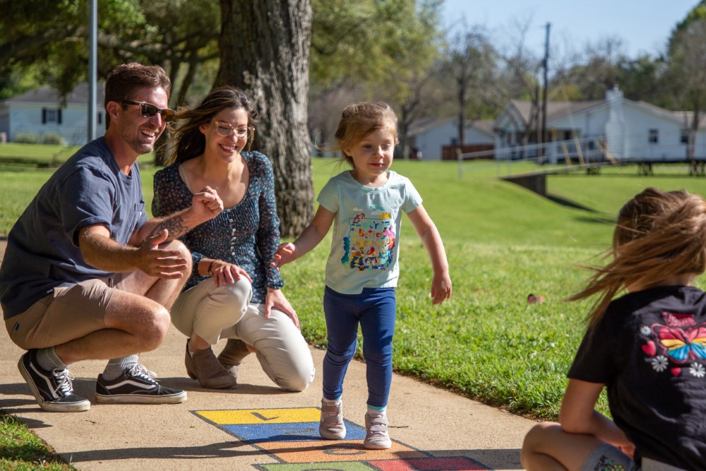 a young child, encouraged by her family, trying out hopscotch on the Born Learning trail in Jackson Street Park