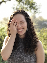 Gina in front of some greenery, laughing.