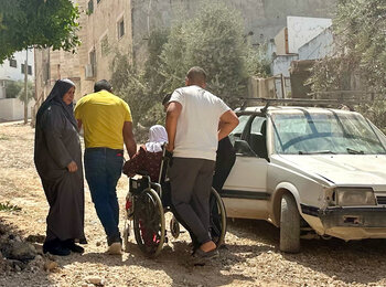 امرأة فلسطينية مسنّة على كرسي متحرك تتنقل في شارع مدمر في جنين في طريقها إلى المستشفى، عقب عملية نفذتها القوات الإسرائيلية على مدار عشرة أيام. تصوير مكتب الأمم المتحدة لتنسيق الشؤون الإنسانية، 8 أيلول/سبتمبر 2024