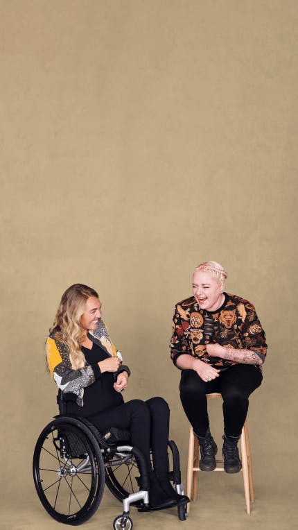 Woman in wheelchair sat next to another woman on chair both laughing