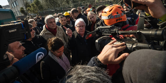 Crowds of people with cameras and microphones surround a gray-haired man.