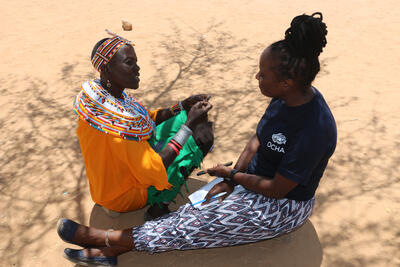 Two women sat on the ground speaking with one another