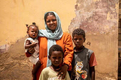 A woman stands with a little girl in her arms facing the camera with two young boys standing next to her