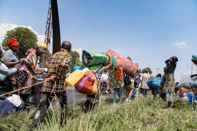 People with bags on the road. People with baggage are also standing on the wayside.