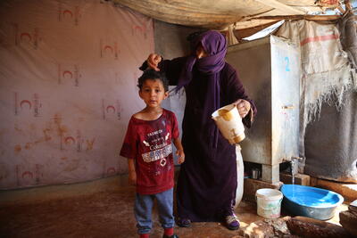 A woman pours water over a child to help him cope with the heat in Al-Hamra camp for internally displaced people in Syria’s Idleb governorate. Photo: OCHA/Bilal Al-Hammoud