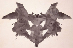 An abstract, freeform, vertically symmetrical, black inkblot on a light background.