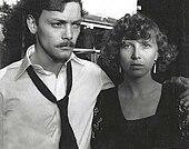 Photo noir et blanc d'un homme moustachu avec une cravate largement desserrée et d'une femme aux cheveux bouclés avec une frange.