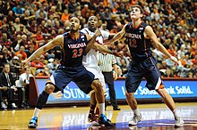 A college basketball player dressed in white with orange and blue bordering prepares to shoot a free throw.