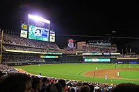 Nighttime shot of a green ball field and large scoreboard and flood lights lit up behind it