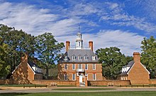 A three-story red brick colonial-style hall and its left and right wings during summer.