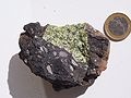 Peridotite (green) mantle xenolith within a (dark) volcanic bomb from Vulkaneifel, Germany (coin of one euro for scale)