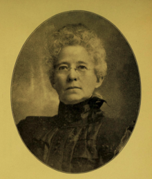 B&W oval portrait photo of a white-haired old woman wearing a high-collared dark blouse.