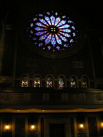 Stained glass rose window over balcony overlooking the pews.