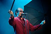 A man in a red suit holding a cane and an umbrella, singing into a microphone stand