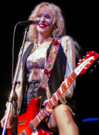 Woman playing guitar, with her left leg up on a monitor.