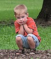 Young boy squatting in a park.