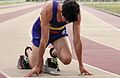 Sprint runner preparing to start race using starting blocks – upper body tilted forwards.