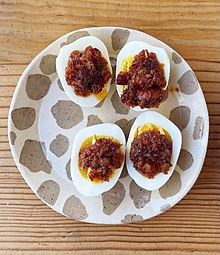 Two soft boiled eggs split in half. Each half has XO sauce on top of it.