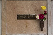 Photo of Monroe's crypt, taken in 2005. "Marilyn Monroe, 1926–1962" is written on a plaque. The crypt has some lipstick prints left by visitors and flowers are placed in a vase attached to it.