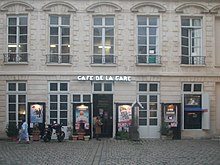 Photographie d'une façade d'un bâtiment parisien avec des lettres lumineuses « Café de la Gare » et des affiches de spectacles.