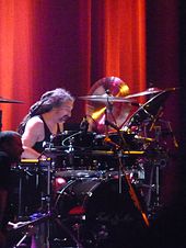 A man with long dreadlocks playing the drums on stage