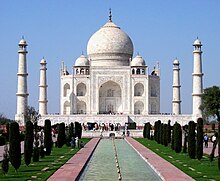 A white stone building with three domes flanked by a wall and four towers