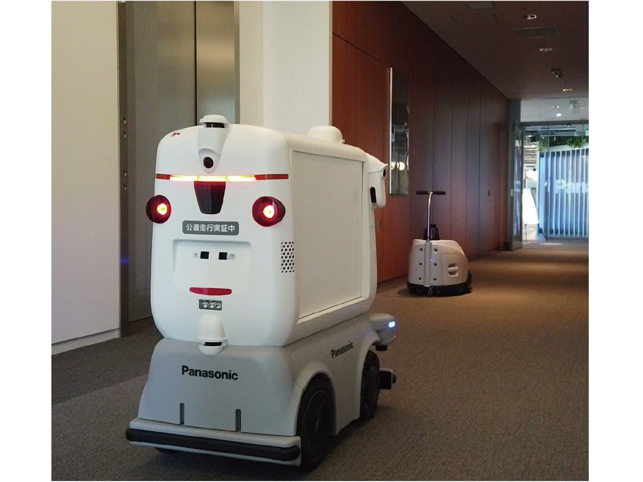 A transport robot and a cleaning robot are running automatically through the passage in the building.