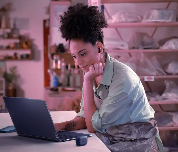 A college-aged female sits at a desk, wearing noise-cancelling headphones while engaged in a virtual class.