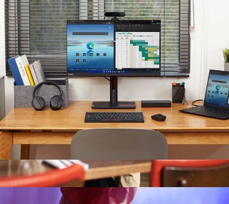 A brightly lit office desk featuring Lenovo products including a ThinkVision monitor, ThinkPad laptop, and accessories.