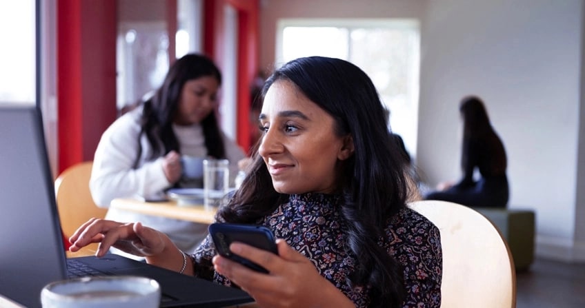 A woman in a cafe entering the code from her mobile phone into her laptop computer