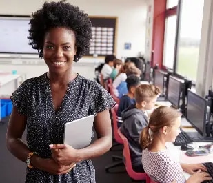 A teacher stands at the front of a classroom in front of her students.