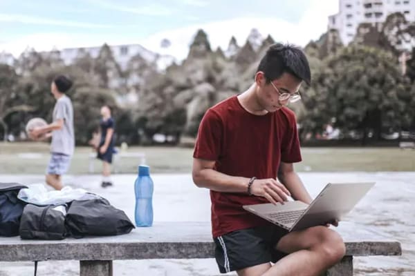 A man sitting beside a basketball court using a Lenovo laptop