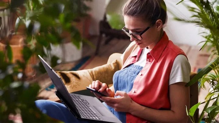 A woman with her laptop on her lap and phone in her hand