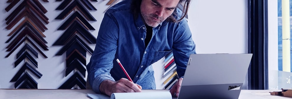 A man sitting at a desk working on a ThinkBook laptop with open lid