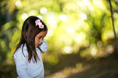 A small girl is standing outdoors. Lights on the backgound are blurred