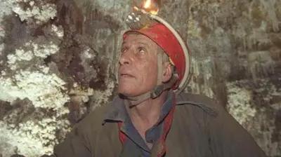 Fotografia mostra homem branco em roupas de escaladas dentro de uma caverna