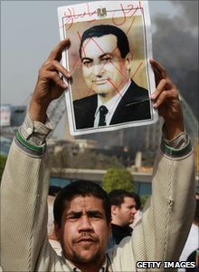 A protester in Tahrir Square holds a photo showing President Mubarak's face crossed out, 29 January