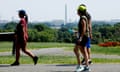 People wearing shorts, sneakers, hats, and carrying water bottles walk outside with the Washington monument visible in the distance