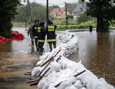 Firefighters and volunteers stand near a line of sandbags on a wet street