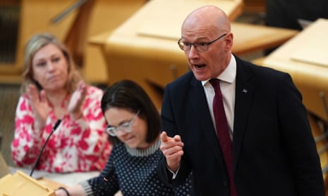 John Swinney delivers a statement at Holyrood: he has a hand raised and looks animated as one woman claps in the background and another looks down at her notes