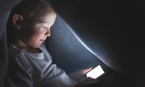 A child under a blanket playing with a smartphone