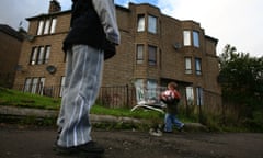 STwo young boys play football in a run down street with boarded up houses