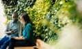 Businessman and woman sitting in front of green plant wall, using laptop