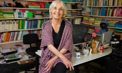 Anne Fine sits on the edge of a desk in a room lined with books on shelves