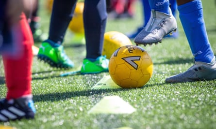 Unidentifiable children at football training: view of feet and legs in brightly coloured socks and a yellow football